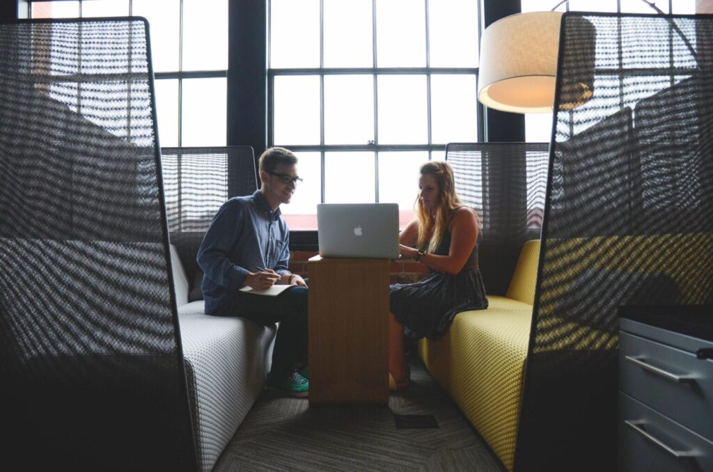 A man and a woman are looking into a laptop and are taking notes.