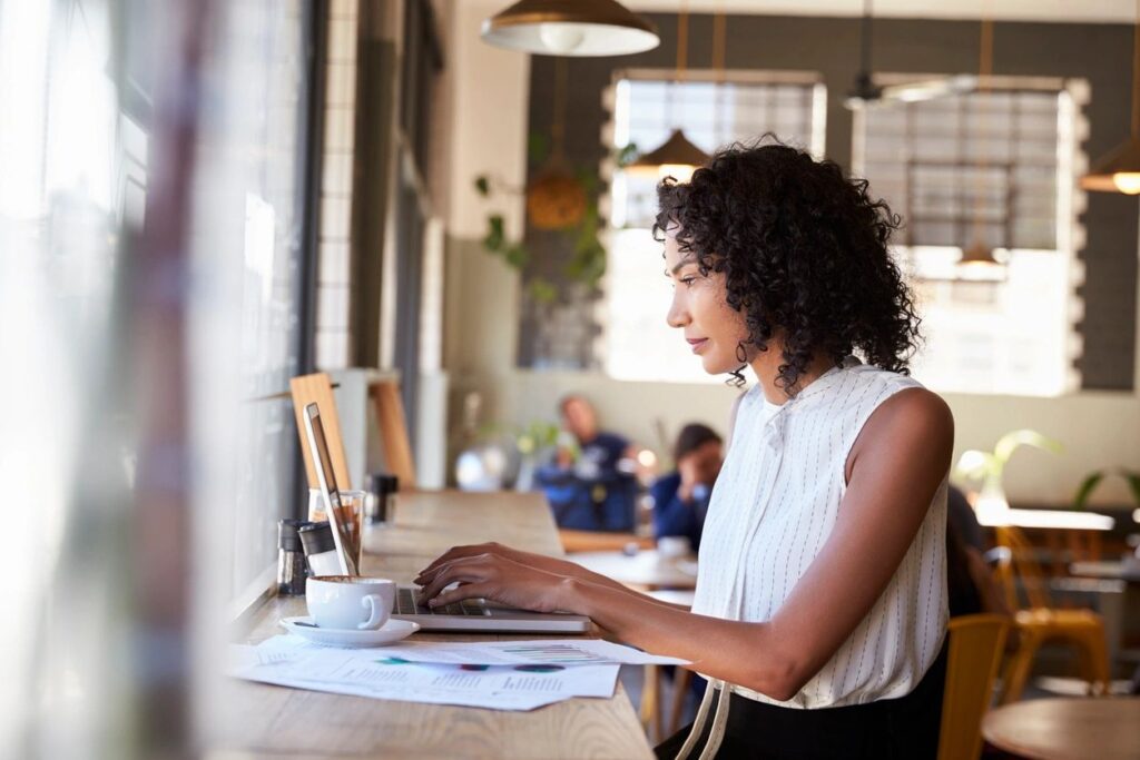 A woman is sitted at a corner while typing on her laptop.